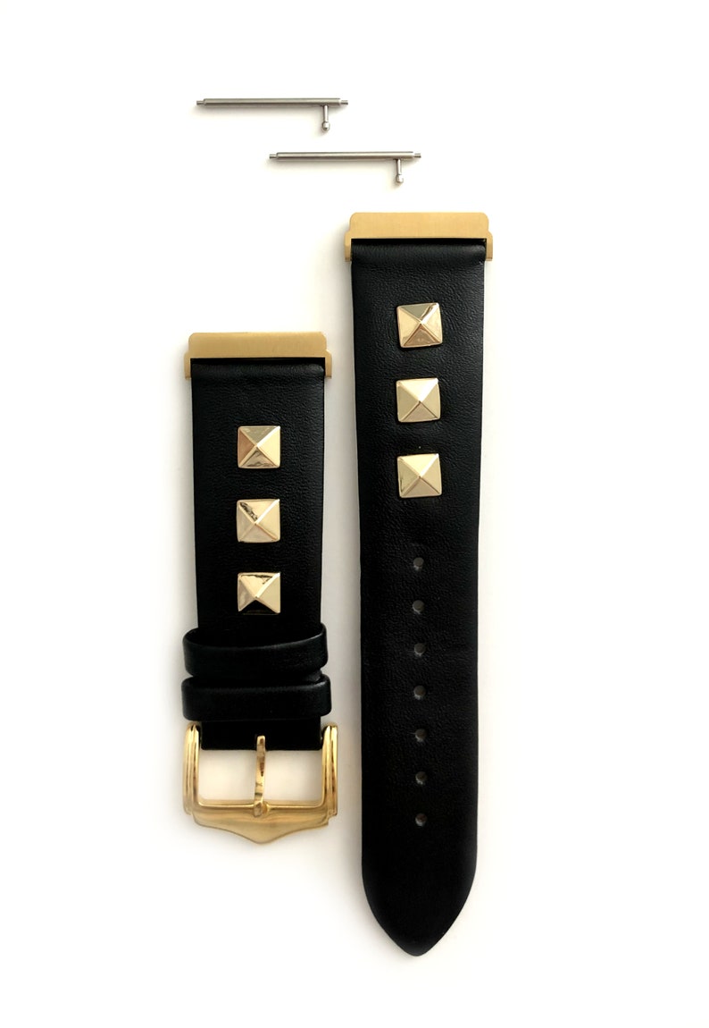 May include: Black leather watch band with gold-tone studs and a gold-tone buckle. The band is shown with two spring bars.