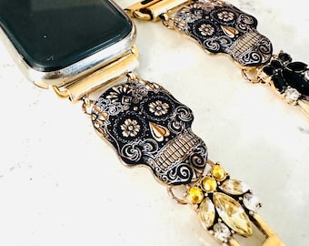 Könnte beinhalten: Goldenes Armband mit einem schwarzen und goldenen Zucker Schädel-Anhänger. Das Armband ist aus Metall und hat einen Verschluss. Der Anhänger ist mit komplizierten Designs verziert und hat eine schwarze Emaille-Oberfläche.