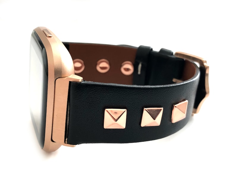May include: A black leather watch band with rose gold accents and pyramid-shaped studs. The band is designed for a square-shaped smartwatch.