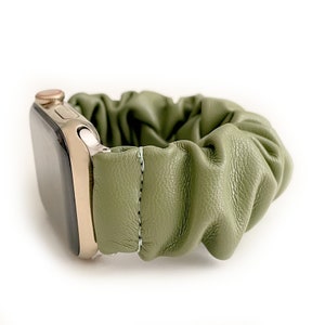 Op de afbeelding: Een olijfgroene leren scrunchie horlogeband gecombineerd met een goudkleurige smartwatch. De band is gerimpeld en gestikt, waardoor een textuurrijke, stijlvolle look ontstaat. De wijzerplaat van het horloge is zwart.