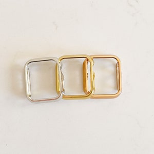 May include: Three square watch bands in different colours: silver, gold, and rose gold. The bands are made of metal and have a smooth finish.