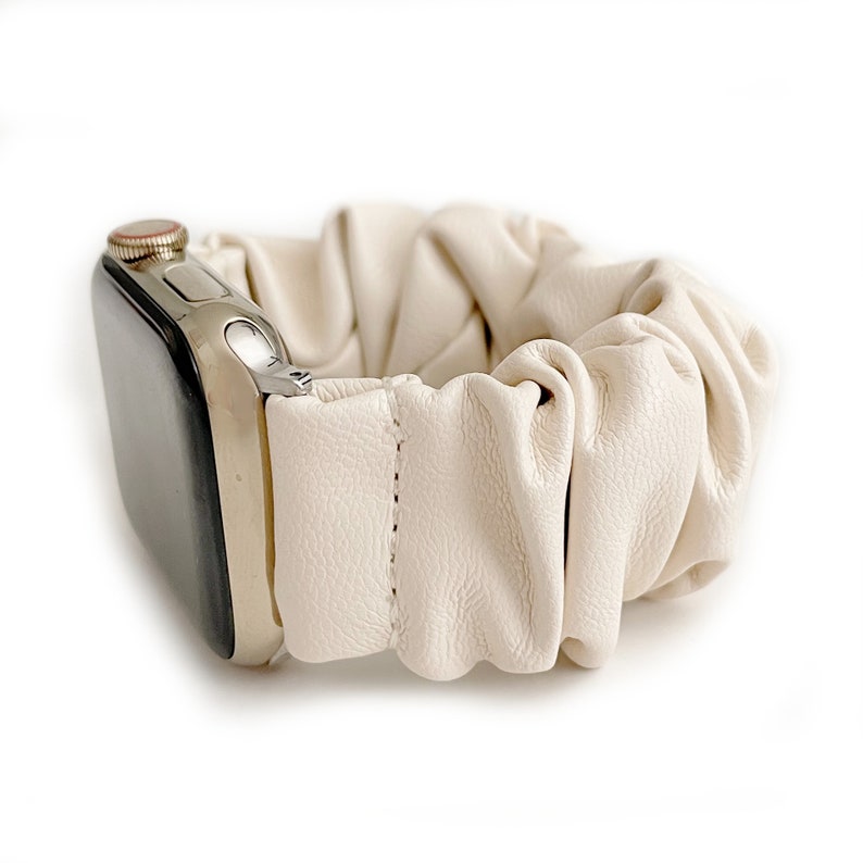Op de afbeelding: Cr&egrave;me-kleurige leren scrunchie horlogeband. De band is bevestigd aan een zilveren Apple Watch. Het scrunchie-ontwerp is geplooid en getextureerd, met een gestikt naaddetail. De wijzerplaat van het horloge is zwart.