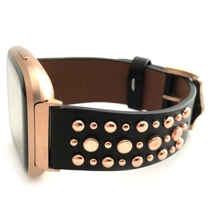 May include: A rose gold smartwatch with a black leather band adorned with rose gold studs.