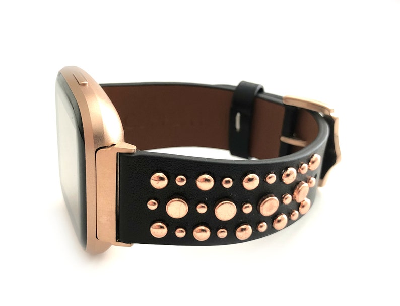 May include: A rose gold smartwatch with a black leather band adorned with rose gold studs.