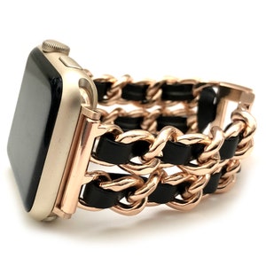 Puede incluir: Una banda de reloj Apple de cadena de oro rosa con detalles de cuero negro. La banda está diseñada para un reloj inteligente.
