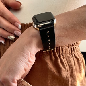 May include: A black leather watch band with gold accents and a black watch face. The band has small gold dots along the edge.