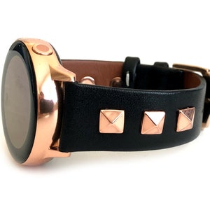 May include: A rose gold smartwatch with a black leather strap featuring rose gold pyramid-shaped studs.