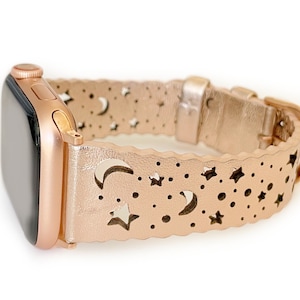 May include: A rose gold Apple Watch band with a cut-out design of moons and stars. The band is made of leather and has a buckle closure.