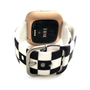 May include: A rose gold smartwatch with a black and white checkered silicone band. The watch face is black and displays the time, date, and heart rate.