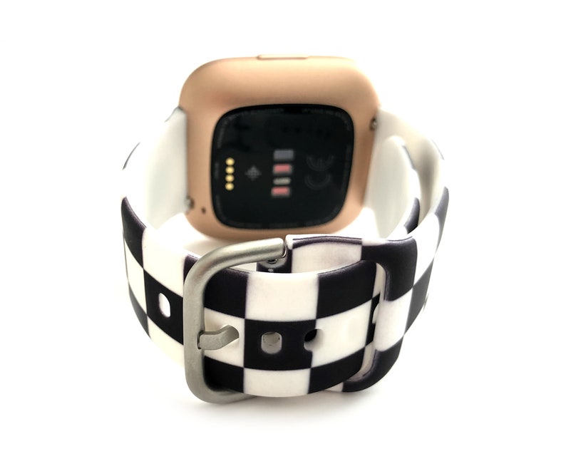 May include: A rose gold smartwatch with a black and white checkered silicone band. The watch face is black and displays the time, date, and heart rate.