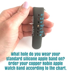 May include: A gray silicone Apple Watch band with a size chart printed on the side. The chart shows sizes from 5 to 8 inches. The text "Copper Robin" is printed vertically on the band.