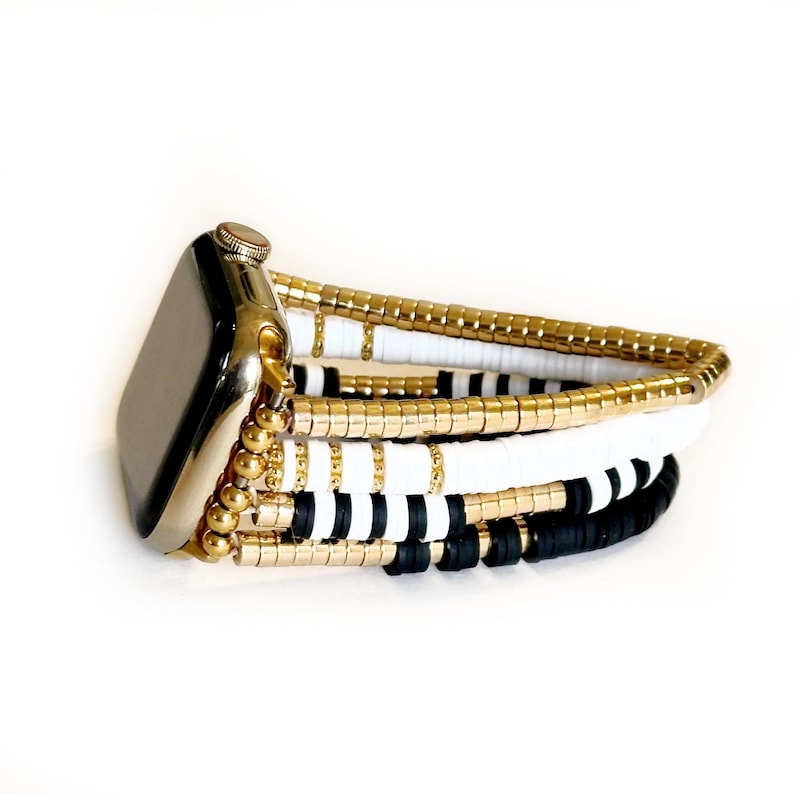 May include: A gold, black, and white beaded Apple Watch band. The band is made of multiple strands of beads, including gold, black, and white beads.