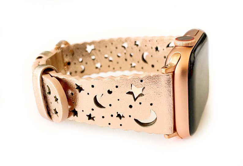 May include: Rose gold Apple Watch band with a cut-out design of stars and moons.