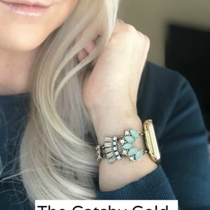 Puede incluir: Una pulsera de reloj dorada con un dise&ntilde;o decorativo que presenta diamantes de imitaci&oacute;n de color azul claro y transparentes. La banda est&aacute; etiquetada como "The Gatsby Gold".