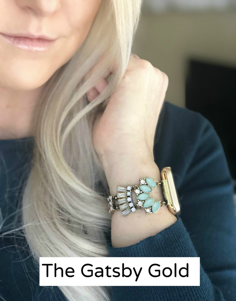 Puede incluir: Una pulsera de reloj dorada con un dise&ntilde;o decorativo que presenta diamantes de imitaci&oacute;n de color azul claro y transparentes. La banda est&aacute; etiquetada como "The Gatsby Gold".