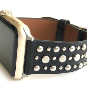 May include: A gold Apple Watch with a black leather band studded with silver rivets.