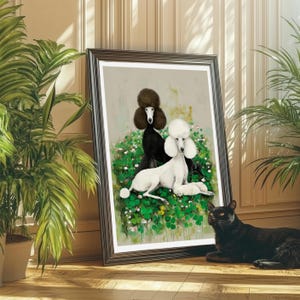 May include: Framed art print featuring two poodles, one black and one white, amidst a bed of green foliage and small white flowers. The poodles are depicted in a classic, elegant style. A black cat is resting on the wooden floor in front of the artwork.