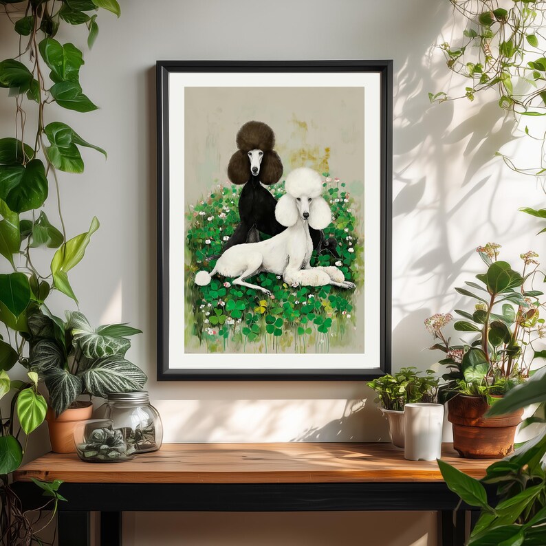 May include: A framed art print featuring two poodles. One poodle is black, the other is white, both with fluffy fur. They are set against a backdrop of green foliage and white flowers. The artwork is displayed on a wooden surface.