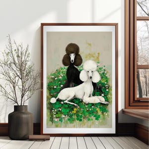 May include: A framed art print featuring two poodles. One poodle is black, the other is white, and they are set against a backdrop of green foliage and small white flowers. The artwork is displayed in a room with natural light.