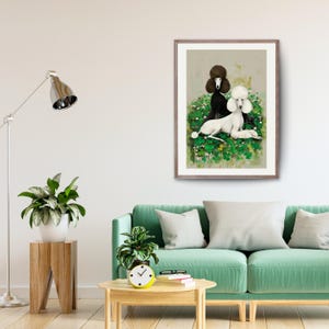 May include: Framed art print featuring two poodles. One poodle is black, the other is white, both with fluffy fur. They are set against a backdrop of green foliage and small white flowers. The artwork is displayed in a living room setting.