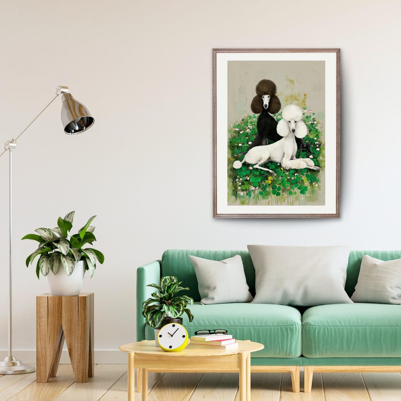May include: Framed art print featuring two poodles. One poodle is black, the other is white, both with fluffy fur. They are set against a backdrop of green foliage and small white flowers. The artwork is displayed in a living room setting.