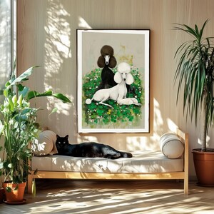 May include: A framed art print featuring two poodles, one black and one white, resting in a bed of green clover. A black cat lounges on a wooden daybed in front of the artwork. The room has a natural, sunlit ambiance with potted plants.