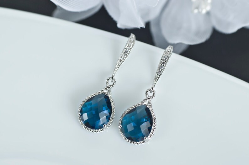 K&ouml;nnte beinhalten: Ein Paar silberne Ohrh&auml;nger mit tropfenf&ouml;rmigen blauen Edelsteinen. Die Ohrringe haben ein zartes, gedrehtes Design.