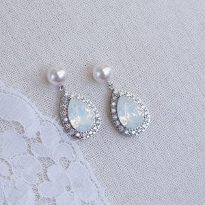 May include: A pair of silver teardrop earrings with a white opal stone and a pearl accent.
