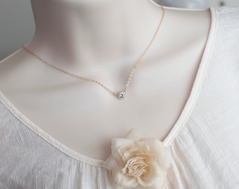 May include: A delicate gold chain necklace with a single, clear round gemstone pendant.