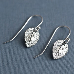 May include: A pair of silver earrings with a leaf design. The leaves are textured and have a delicate, organic look.