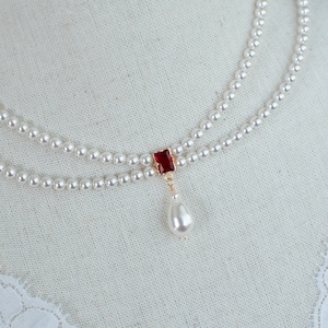 May include: A two-strand pearl necklace with a red gemstone pendant and a single pearl drop.