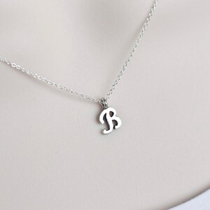 May include: A silver chain necklace with a silver pendant in the shape of the letter B.