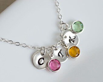 May include: Silver necklace with four charms, each with a letter and a gemstone. The gemstones are green, yellow, pink, and clear.