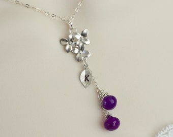 May include: A silver necklace with a cluster of small silver flowers, a silver leaf with the letter "K" engraved on it, and two dangling purple gemstones.