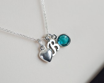 May include: A silver necklace with three charms: a heart, a letter 'B', and a teal blue crystal.