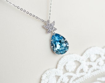 Puede incluir: Un collar de plata con un colgante de cristal azul en forma de lágrima y un pequeño dije de estrella de mar con cristales transparentes.