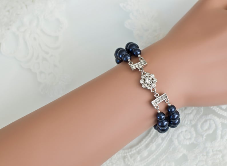 K&ouml;nnte beinhalten: Ein Armband mit zwei Reihen dunkelblauer Kunstperlen, einem silbernen Verschluss und einem silbernen Strassstein-Anh&auml;nger.