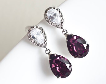 May include: A pair of silver teardrop earrings with a clear crystal on top and a purple crystal on the bottom.