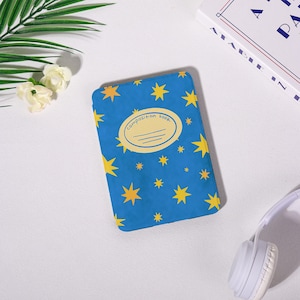 Peut inclure: Un cahier bleu avec un motif d'étoiles jaunes. La couverture porte les mots "composition book" dans un ovale blanc. Le cahier est rectangulaire et semble fermé.