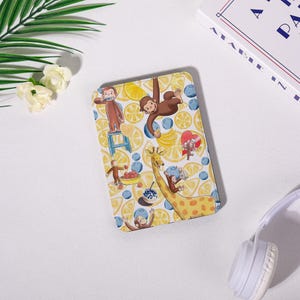 May include: A rectangular case with a fun design featuring a brown monkey, a giraffe, and various fruits like lemons and blueberries. The background is bright yellow, creating a cheerful and whimsical aesthetic.