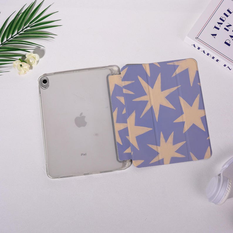 K&ouml;nnte beinhalten: Ein iPad in einer transparenten H&uuml;lle mit einer blauen und beigefarbenen Sternmuster-Abdeckung. Das iPad ist ge&ouml;ffnet und zeigt den Bildschirm. Die Abdeckung ist ge&ouml;ffnet und zeigt ein sich wiederholendes Sterndesign. Der Hintergrund ist wei&szlig;.
