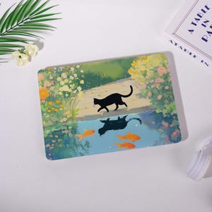 May include: A decorative rectangular item featuring a black cat walking on a path, with its reflection in water below. The water contains orange fish. The background shows flowers and greenery. The item is on a white surface.