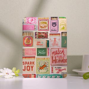 May include: A rectangular collage of vintage matchbox designs. The boxes feature illustrations of a tiger, cat, and lobster, with text including "Spark Joy" and "Match Made in Heaven". The design has a retro aesthetic.