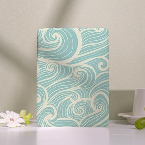 Könnte beinhalten: Ein rechteckiger Gegenstand mit einem türkis- und cremefarbenen Wellenmuster. Das Design zeigt wirbelnde Linien, die an Meereswellen erinnern. Der Gegenstand befindet sich vor einem neutralen Hintergrund mit einer Blume und einer Tasse.