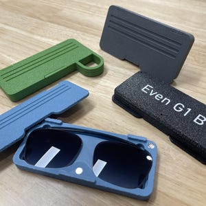 May include: A blue and gray folding sunglasses case with a black case labeled "Even G1 B". There are two other cases, one green and one gray, in the background.