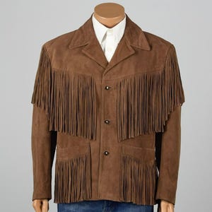 May include: Brown suede jacket with fringe detailing across the chest, shoulders, and pockets. The jacket has a classic western style with a button-up front and a collared neckline. The jacket is displayed on a mannequin.