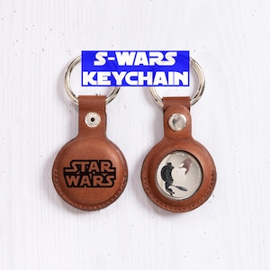 May include: Two brown leather keychains with silver key rings. One keychain has the words "STAR WARS" engraved. The other keychain has a black and white image. The text "S-WARS KEYCHAIN" is in a blue rectangle.