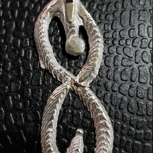 May include: A silver infinity symbol pendant necklace with a textured surface. The pendant is on a silver chain.