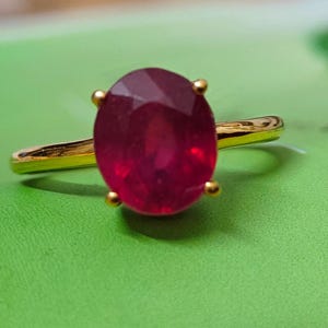 Peut inclure: Une bague en or ornée d'un grand rubis de forme ovale. Le rubis est d'un rouge profond et est maintenu par quatre griffes en or. L'anneau de la bague est également en or.