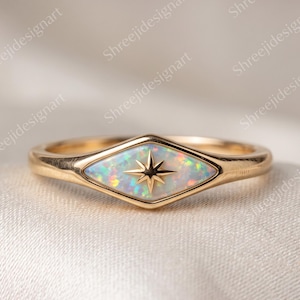May include: A gold ring featuring a marquise-shaped opal inlay with a central eight-pointed star engraving. The iridescent opal displays flashes of green, orange, and blue, set within a polished gold band that tapers toward the back.